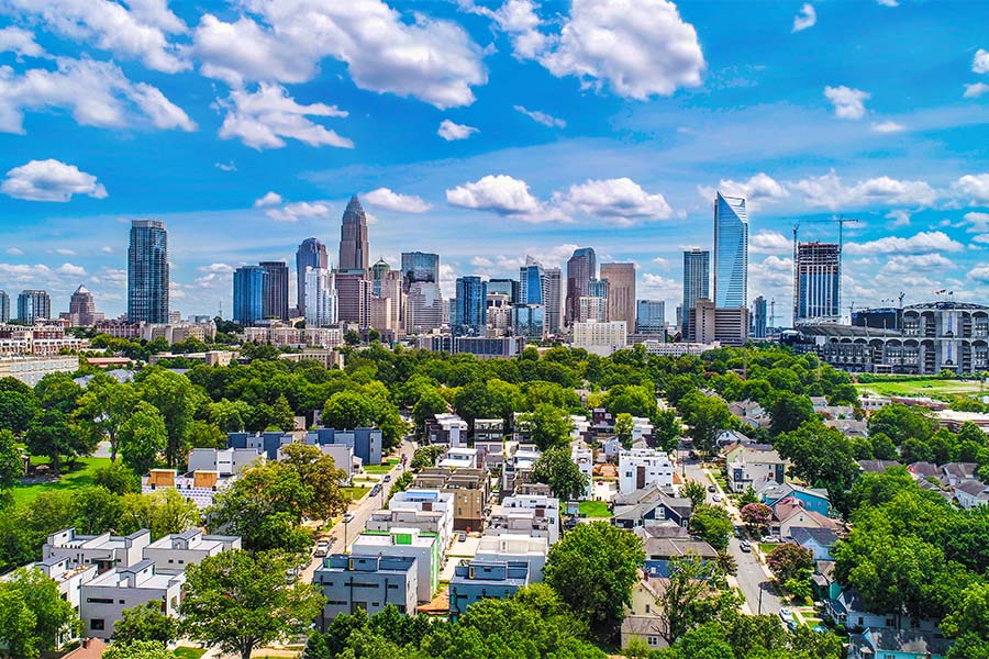 Contact - Aerial View of Charlotte North Carolina City Skyline Against a Vibrant Blue Sky with Views of Commercial Buildings and Homes Surrounded by Green Trees