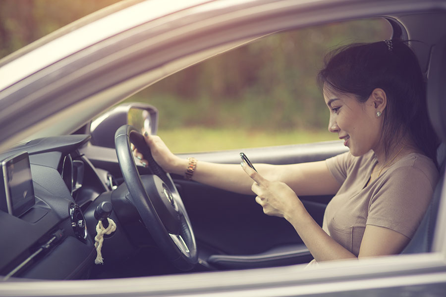 Distracted Driving - View of a Young Distracted Female Driver Using a Phone While Driving in Her Car on a Sunny Day